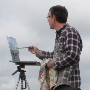 Colin Willey painting outdoors on a hilltop, brush raised to a small canvas on a field easel under a grey sky