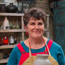 Diana Parker at the wheel in her studio, smiling, shelves of glazed pots behind her
