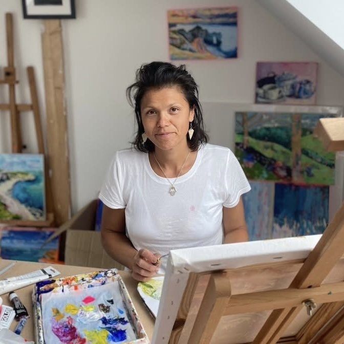 Erica Fairhurst in her studio at a stretcher frame, her paintings stacked and hung on the wall behind