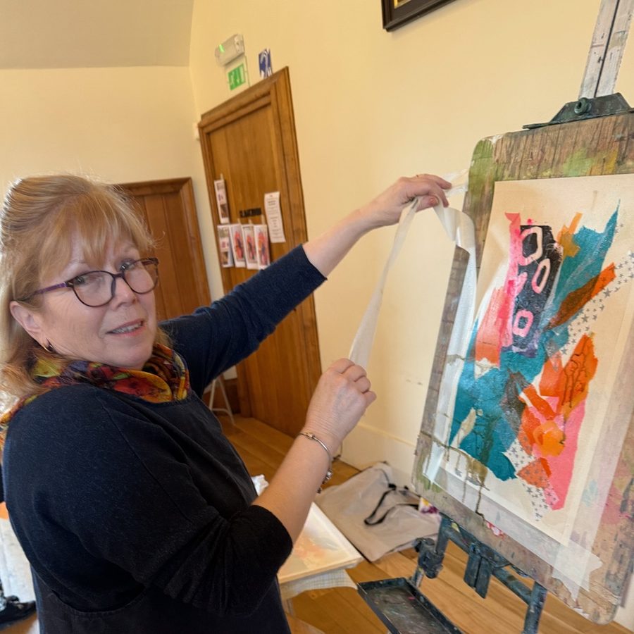 Judy Tate at the press, lifting a freshly printed sheet in pink, orange and turquoise from the plate