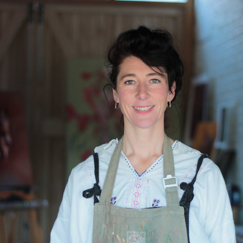 Michelle McCullagh in her studio in a paint-marked apron, canvases propped against the wall behind her