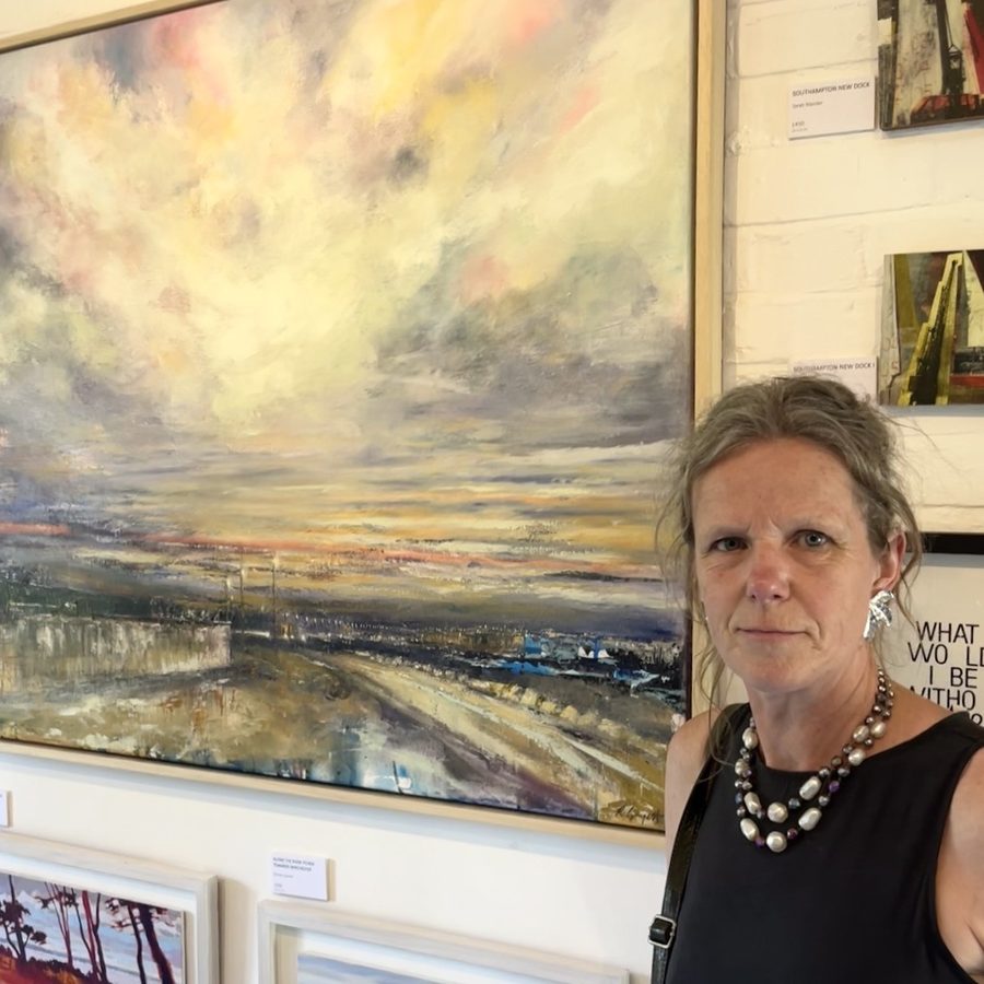 Rebecca Guyett beside one of her large oil paintings — a wide, pale sky over an estuary at dusk