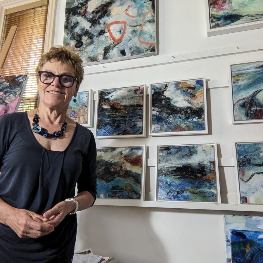 Stella Bawden-Hollis in her studio, in front of a wall of small blue and black mixed-media abstracts