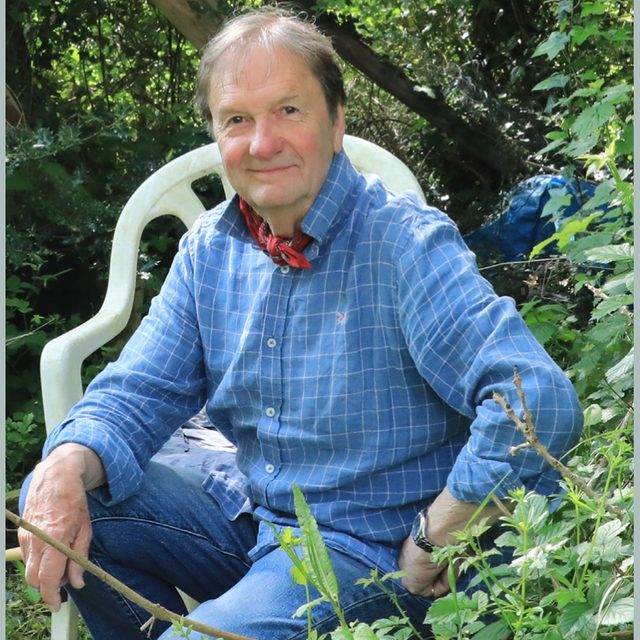 Stephen Calver sitting in a garden chair surrounded by summer greenery