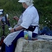 Sue Fawthrop painting outdoors on a clifftop, seated at a field easel with her back to the sea
