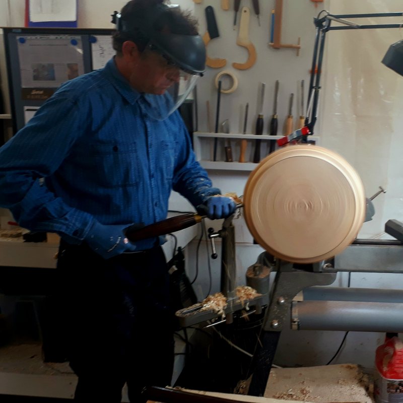 Victor Krause at the lathe in his workshop, turning a broad wooden bowl, tools racked on the wall behind