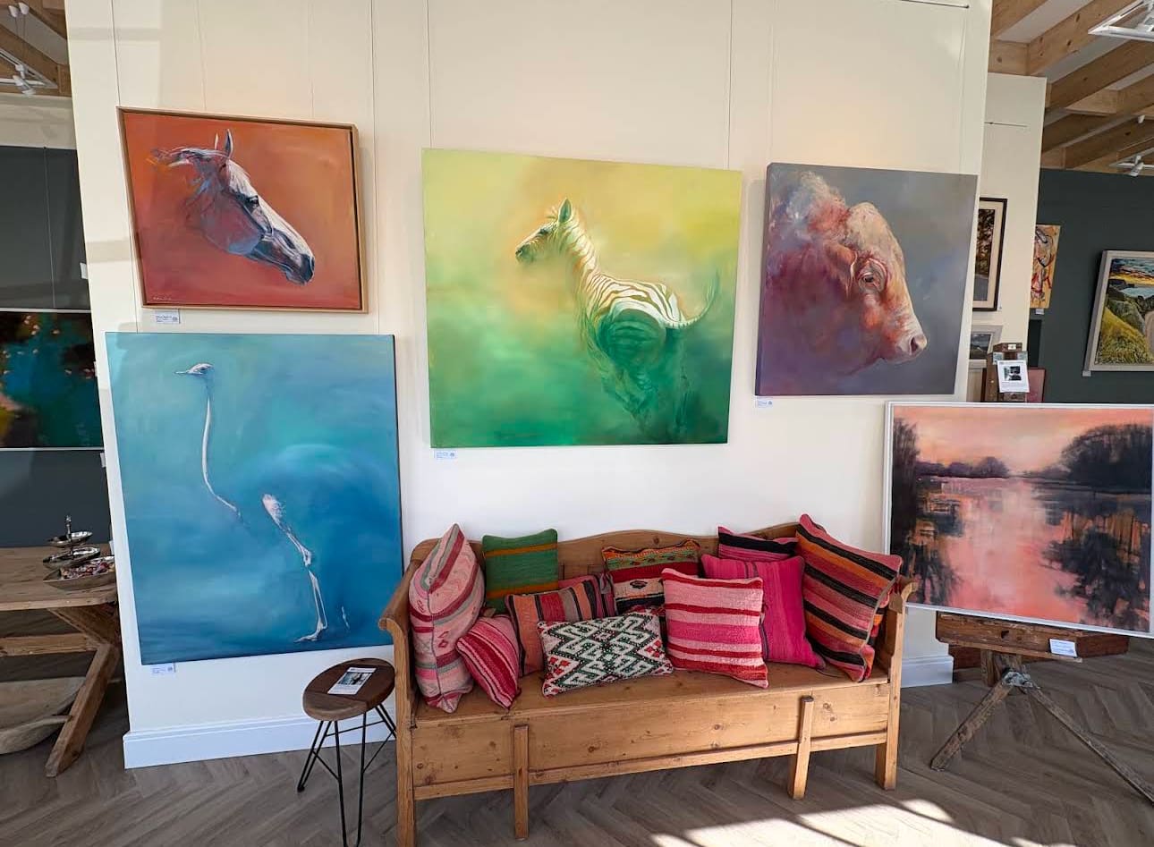 The Moods of Colour hang at The Walnut Gallery — large animal paintings by Michelle McCullagh above a pine bench piled with Moroccan kilim cushions